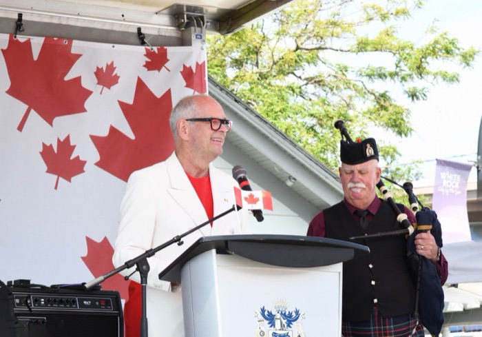Ernie speaking at a community celebration alongside a piper